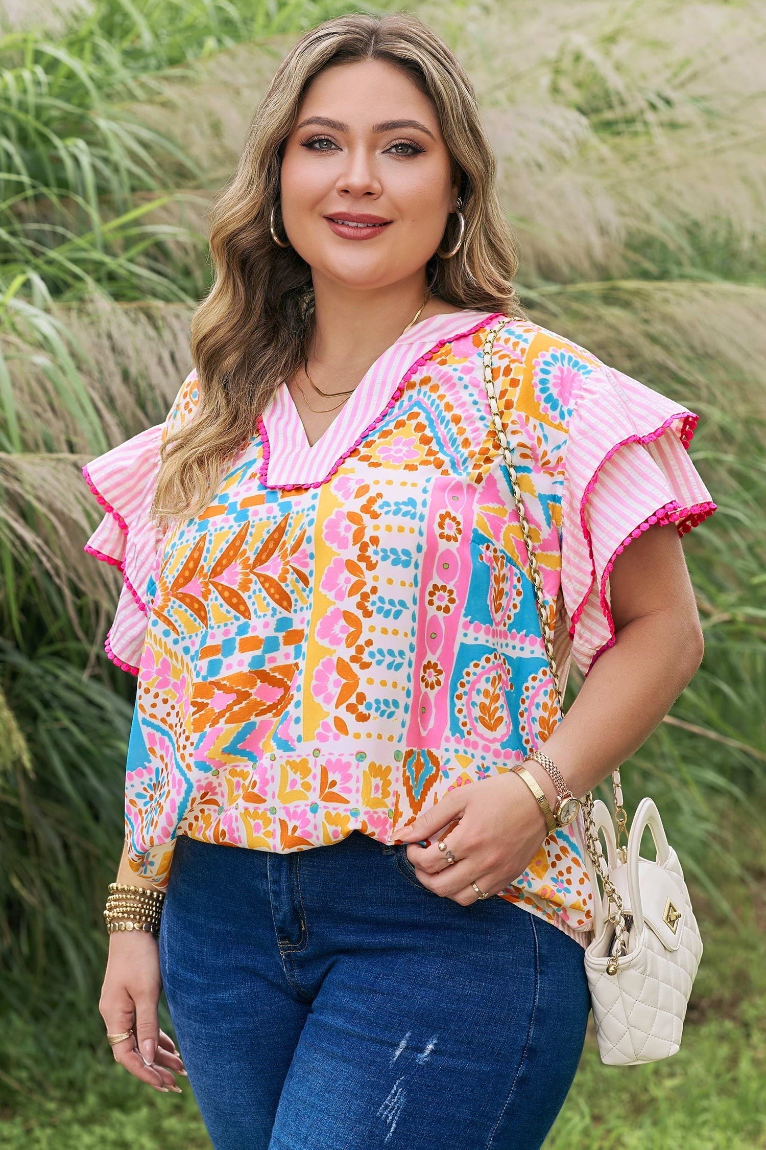 Somethinguluv plus size blouse with vibrant geometric print, V-neck, and pink striped flutter sleeves in a garden.