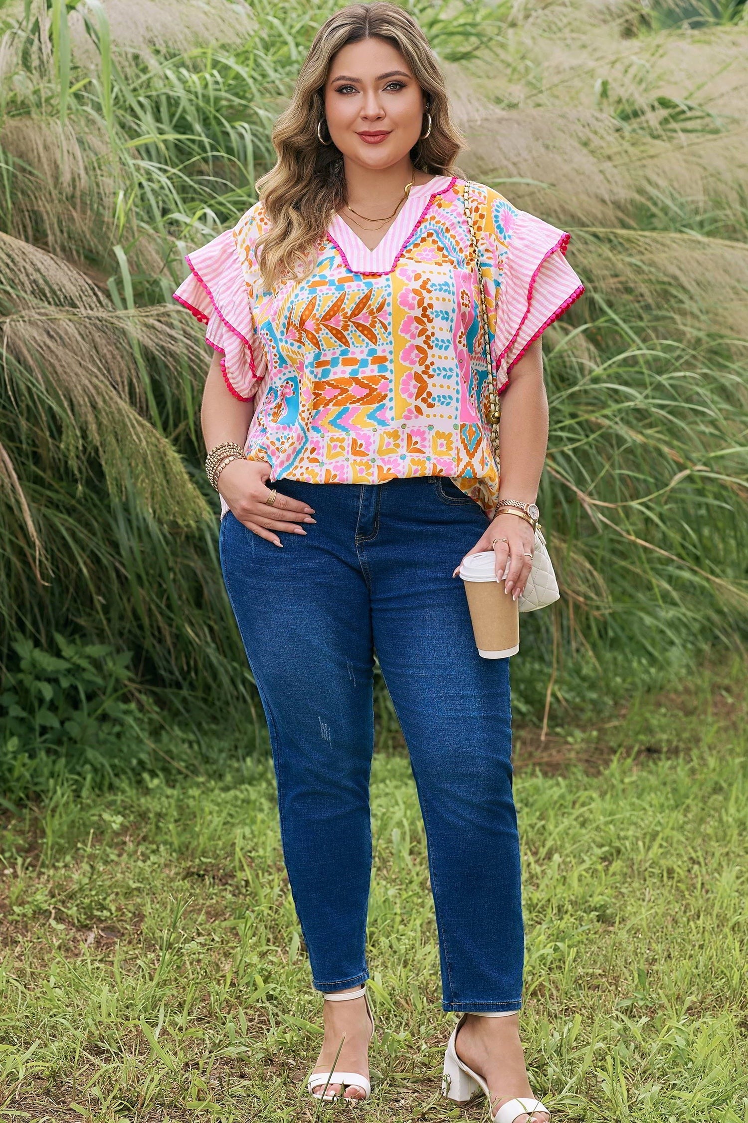 Somethinguluv plus size woman wearing a vibrant geometric print V-neck blouse with ruffled flutter sleeves and jeans.