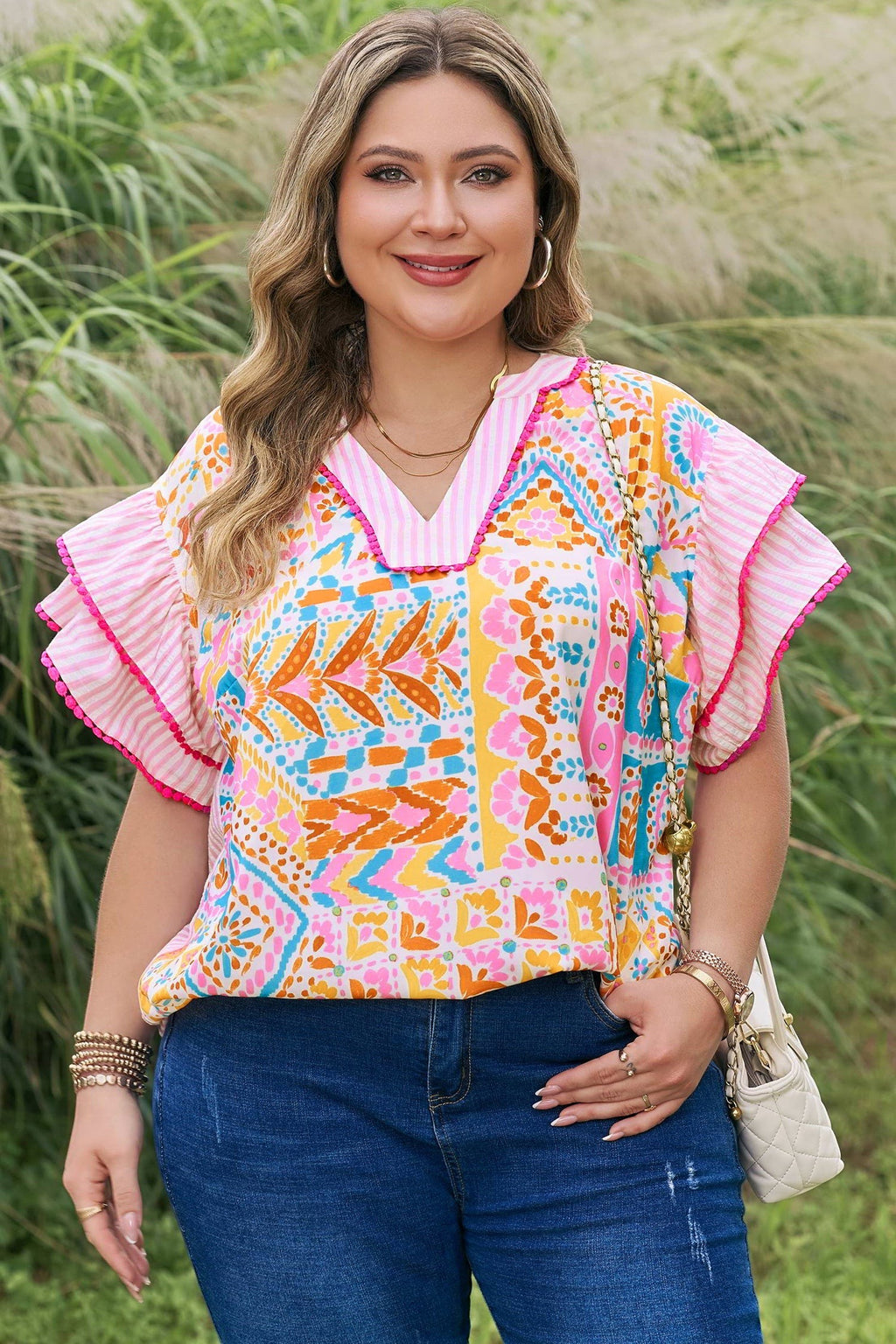 Somethinguluv plus size blouse with vibrant geometric print, V-neck, and pink ruffled flutter sleeves in a garden.