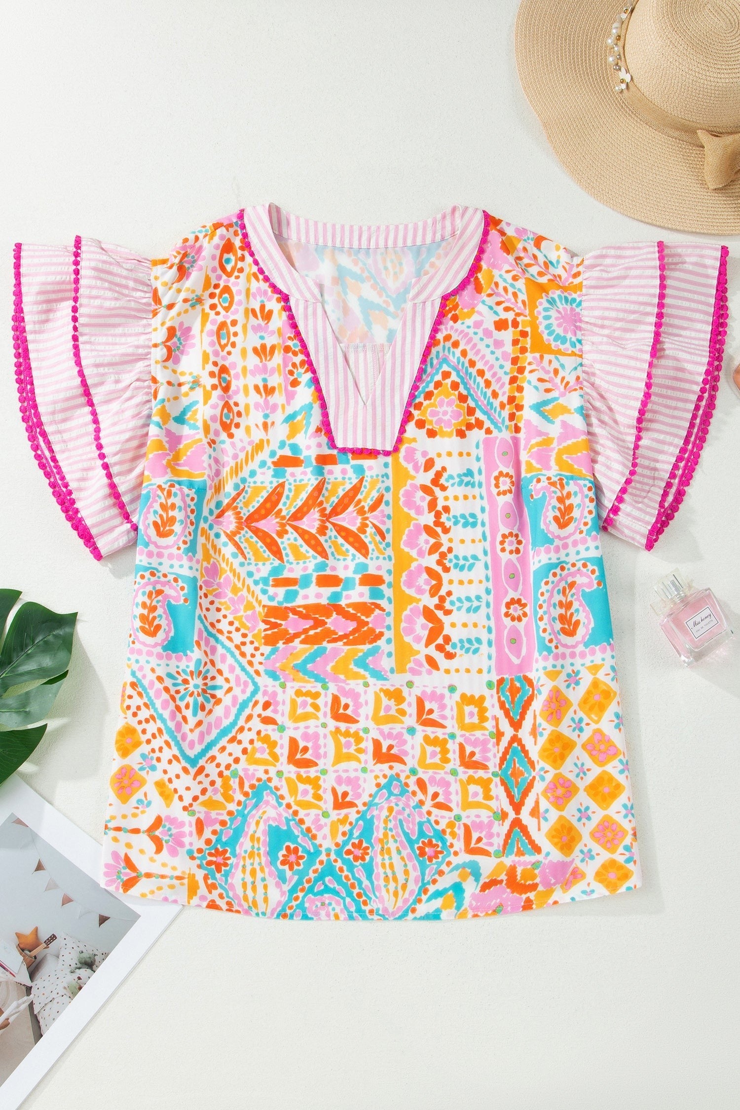 Somethinguluv printed V-neck blouse with flutter sleeves, featuring a vibrant geometric pattern and pink trim details.