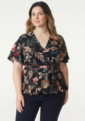 Somethinguluv3 floral print wrap blouse with flutter sleeves and tie waist on a model wearing dark jeans.