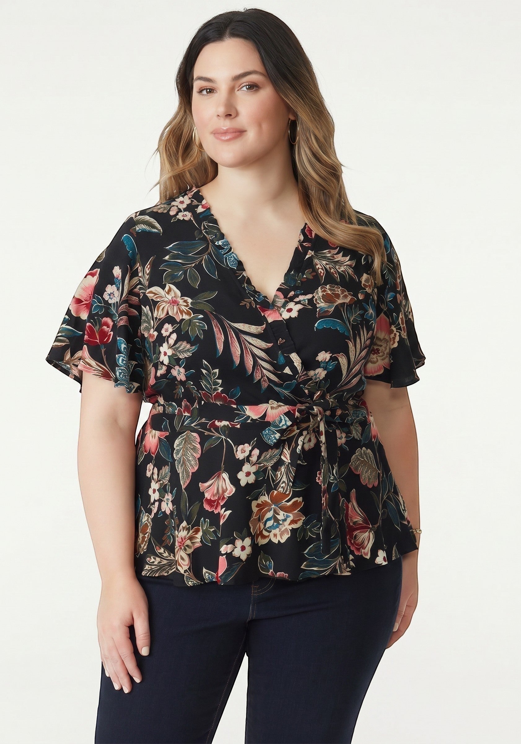 Somethinguluv3 floral print wrap blouse with flutter sleeves and tie waist on a model wearing dark jeans.