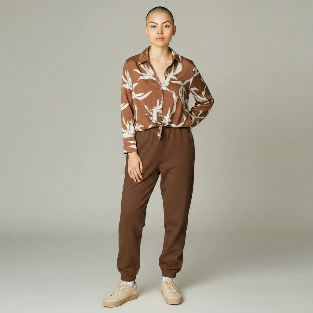 Model wearing a Somethinguluv3 mocha brown long sleeve button-down shirt with a cream abstract leaf print and tie hem.